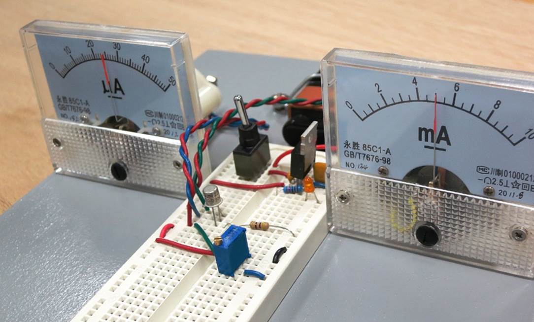 Two analog meters can give an immediate display of the current amplification capability of a basic 2N2222 bipolar transistor. The rectangular blue component in the foreground is a trimmer potentiometer with screw adjustment.