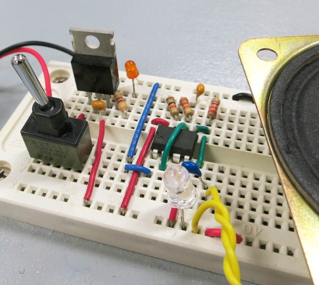 A breadboarded version of the phototransistor test circuit using a 555 timer. The phototransistor is the transparent object at the center near the yellow wires. A loudspeaker is partially visible on the right.
