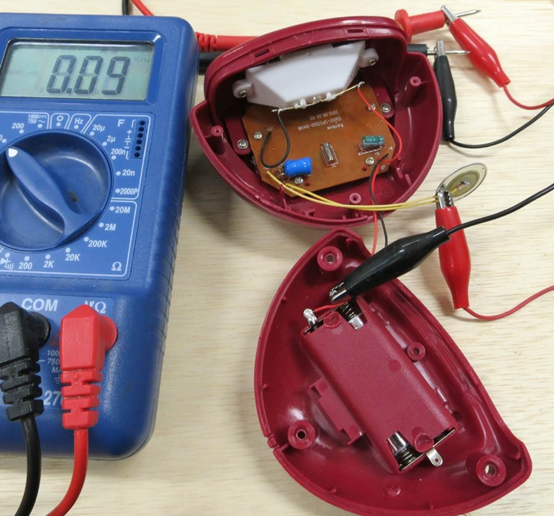 Measuring voltage on the beeper inside a clock, using patch cords with alligator clips to allow hands-free operation. The beeper is the thin, circular object with a red alligator clip gripping one of its solder joints.