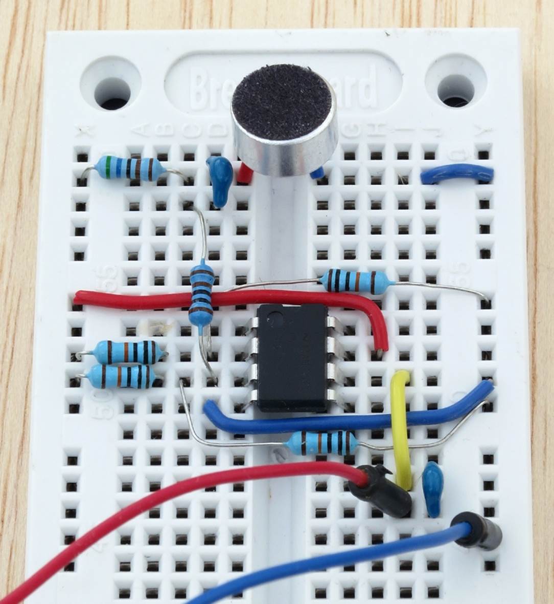 A circuit to assess the amplified output from an electret microphone. The red and blue jumper wires below the circuit are connected with a meter set to measure AC volts. The power supply for the buses of the breadboard is a 9V battery (not shown here).