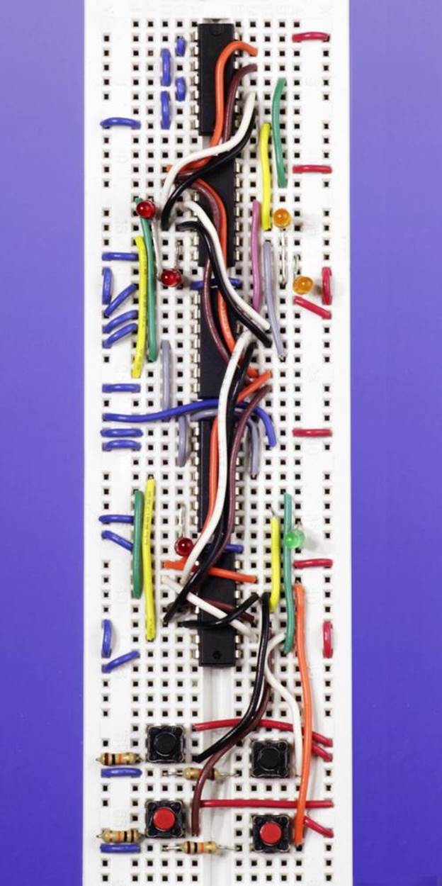 A breadboarded version of the complete Telepathy Test, using five logic chips. Six LEDs provide outputs that are identified in the schematic of the circuit. No series resistors are shown because I chose the type of LED that contains its own series resistor. The two pushbuttons for Player A are the red ones at the bottom. The buttons for Player B are the black ones, immediately above. This configuration of the circuit is only for demonstration purposes. For a functional Telepathy Test, the buttons would be located separately so that the players would be unable to see each other’s choices.Telepathy Testbreadboarded